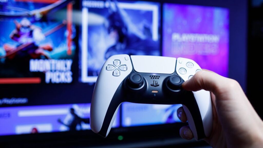 Il DualSense di PS5 in primo piano con sullo sfondo un televisore con dei giochi