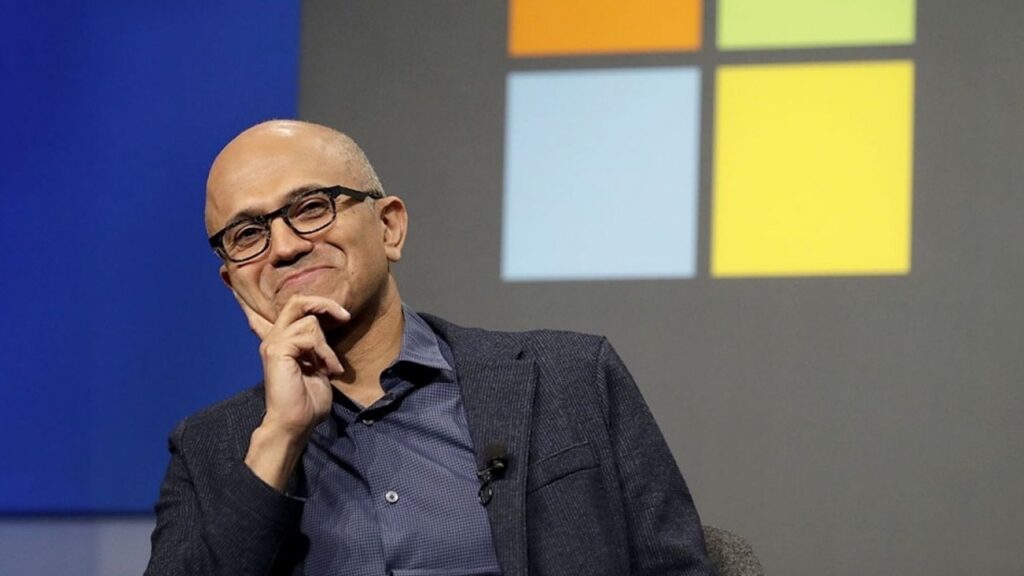 Satya Nadella che sorride e con dietro il logo di Microsoft