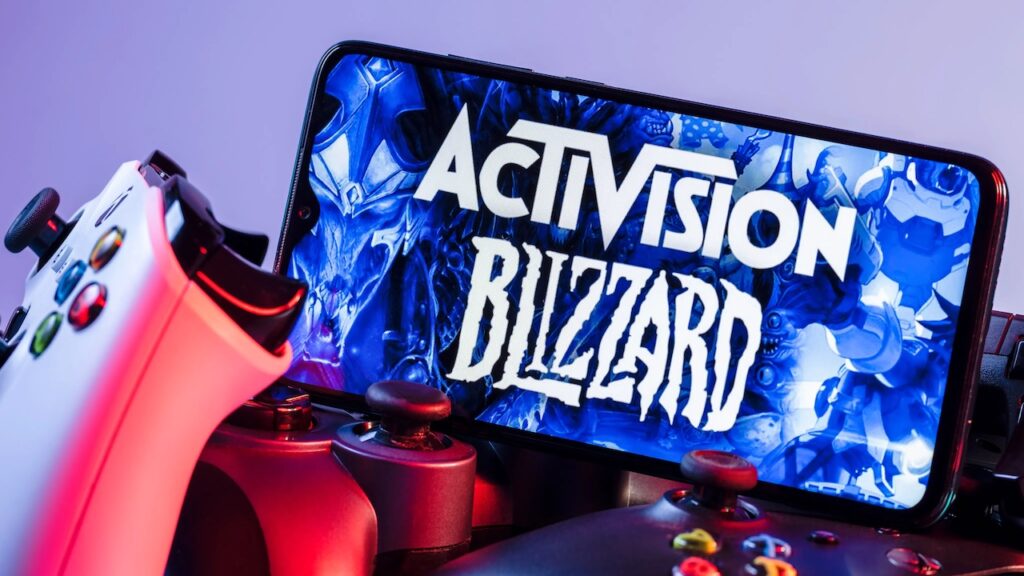 Il logo di Activision Blizzard su uno smartphone con davanti un controller Xbox