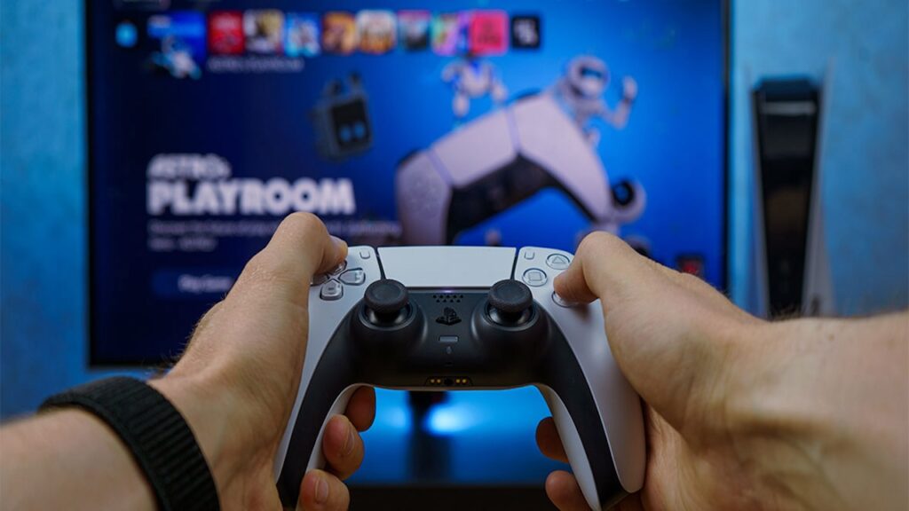 Un DualSense nelle mani di un giocatore con sullo sfondo una PS5