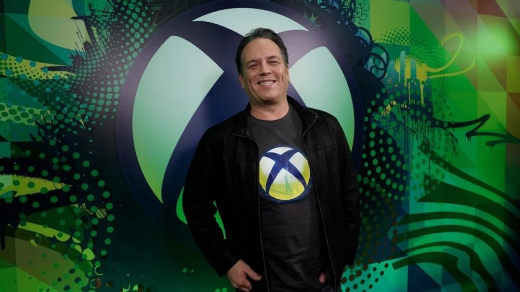 Phil Spencer sorridente con dietro il logo Xbox